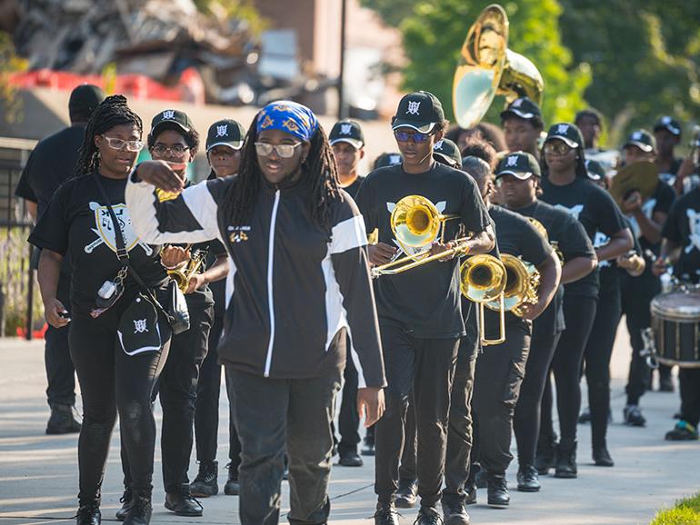 A local high school's band walks together with their instruments on Detroit Mercy's McNichols Campus.