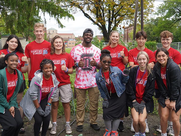 A dozen Detroit Mercy students wearing University of Detroit Mercy t-shirts pose for a photo while participating in community service.